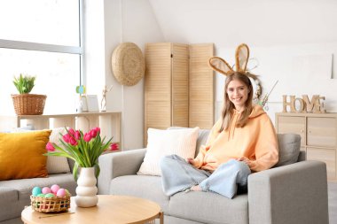 Tavşan kulaklı genç bir kadın evdeki kanepede oturuyor. Paskalya kutlaması