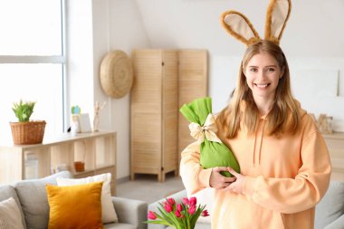 Evde paskalya hediyesi yumurtası olan tavşan kulaklı genç bir kadın.