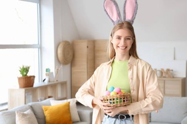 Evde paskalya yumurtası sepeti olan tavşan kulaklı genç bir kadın.