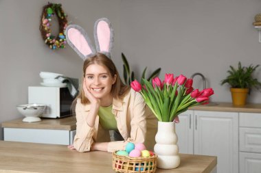 Paskalya yumurtaları ve laleleri evdeki mutfak masasında duran tavşan kulaklı genç bir kadın.