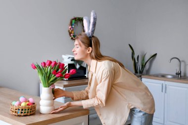 Paskalya yumurtaları ve laleleri evdeki mutfak masasında duran tavşan kulaklı genç bir kadın.