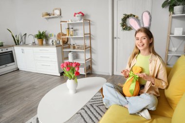 Paskalya hediyesi yumurtası evde oturan tavşan kulaklı genç bir kadın.