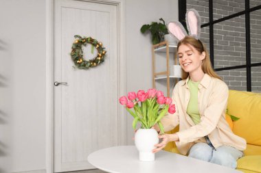 Evde masasında laleler olan tavşan kulaklı genç bir kadın. Paskalya kutlaması