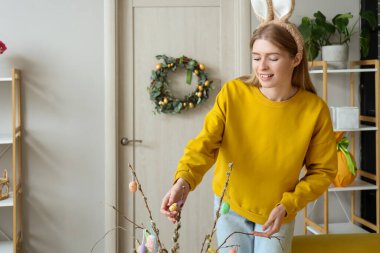 Evde söğüt dalları ve paskalya yumurtaları olan tavşan kulaklı genç bir kadın.