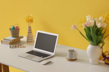 Laptoplu işyeri, Paskalya yumurtaları ve sarı duvarlı çiçekler.