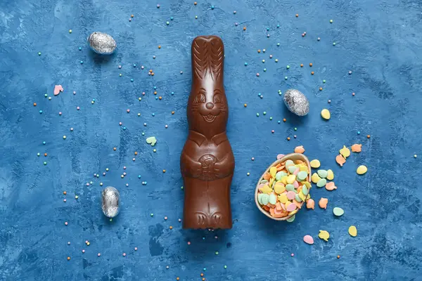Çikolatalı Paskalya yumurtası, mavi arka planda serpiştirilmiş tavşancık.