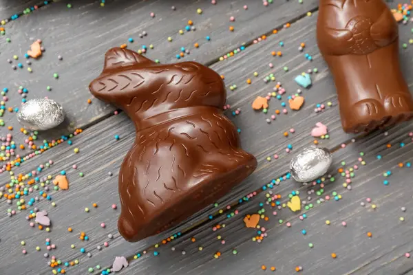 Çikolatalı tavşanlar, folyodaki Paskalya yumurtaları ve gri ahşap arka planda serpiştirmeler.