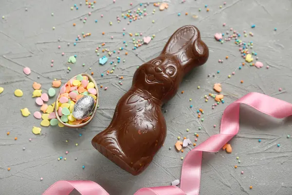 Çikolatalı Paskalya yumurtası, gri arka planda serpiştirilmiş tavşancık.