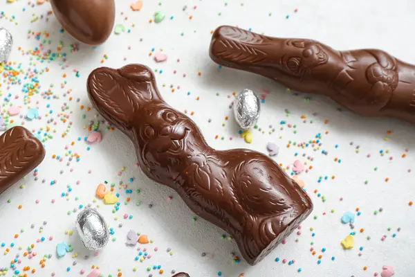 Çikolatalı tavşanlar, folyodaki Paskalya yumurtaları ve beyaz arka planda serpiştirmeler.