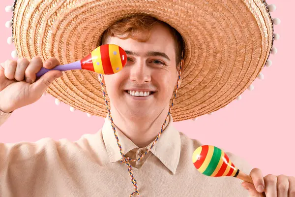 Sombrero 'lu genç Meksikalı adam portresi ve pembe arka planda marakas.