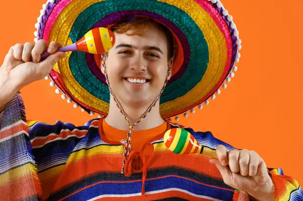 Sombrero 'lu genç Meksikalı adam portresi ve turuncu arka planda marakas.
