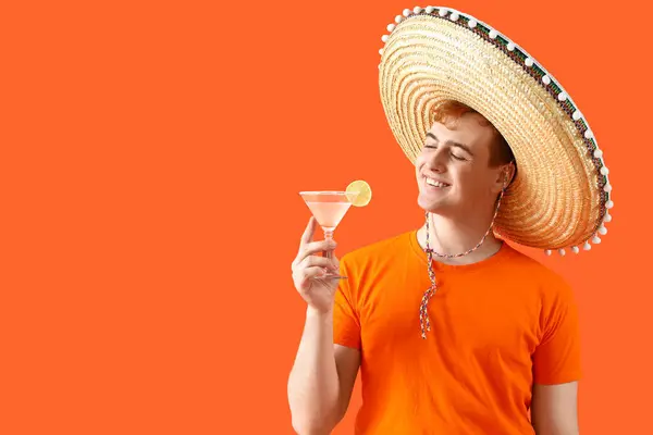 Portrait of young Mexican man in sombrero and with margarita cocktail on orange background