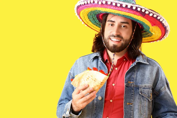 Handsome young Mexican man with taco on yellow background