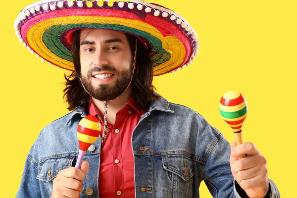 Sombrero 'daki yakışıklı Meksikalı genç adam ve sarı arka planda marakas.