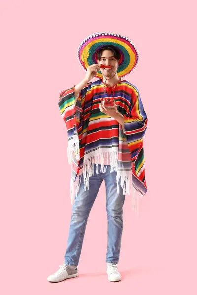 Young Mexican man with chili pepper on pink background