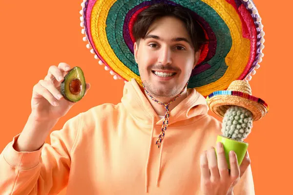 Turuncu arka planda kaktüs ve avokado olan genç Meksikalı adam.