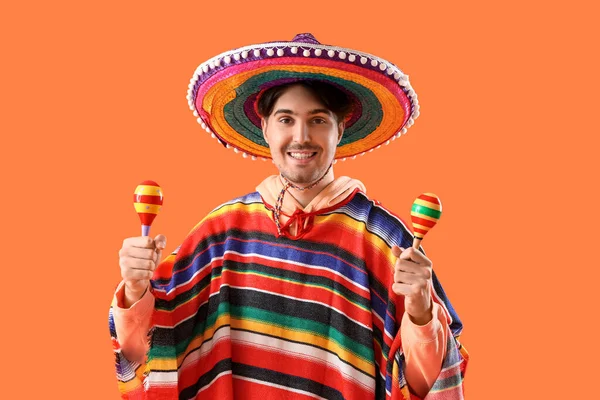 Young Mexican man with maracas on orange background