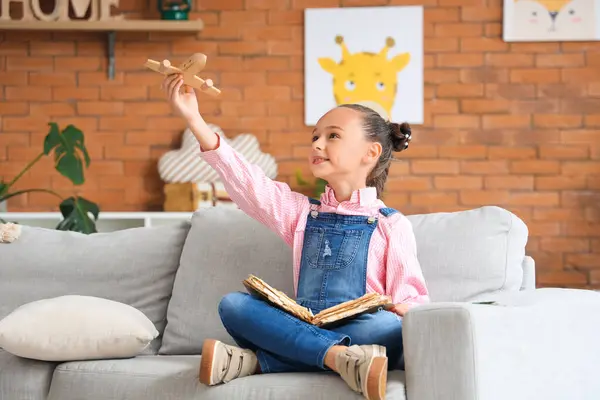 Cute little girl with adventure book and wooden airplane at home