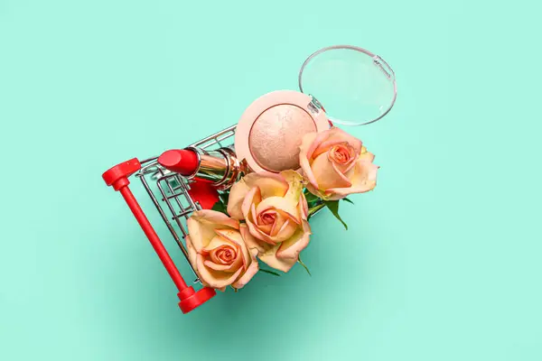 Shopping cart with makeup products and beautiful rose flowers on turquoise background