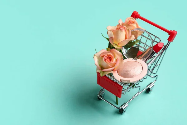 Shopping cart with makeup products and beautiful rose flowers on turquoise background