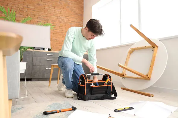 Young man with bag of tools assembling furniture in kitchen