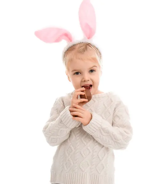 可爱的小女孩在兔子耳朵里吃着白色背景的巧克力蛋 复活节庆祝活动 — 图库照片