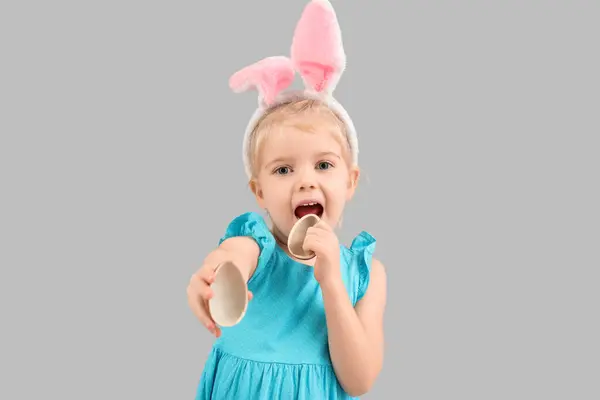 可爱的兔子耳朵小女孩吃着灰色背景的巧克力蛋 复活节庆祝活动 — 图库照片