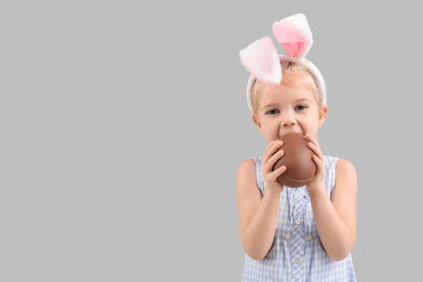 可爱的兔子耳朵小女孩吃着灰色背景的巧克力蛋 复活节庆祝活动 — 图库照片