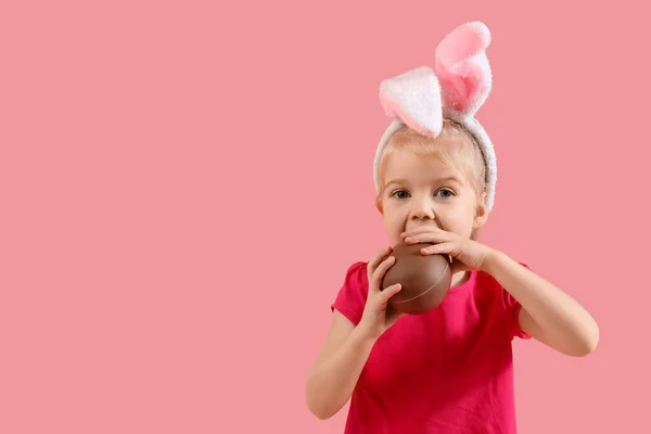 可爱的兔子耳朵小女孩吃粉色背景的巧克力蛋 复活节庆祝活动 — 图库照片