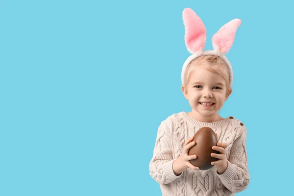快乐的小女孩 戴着蓝色背景的巧克力蛋 长着小兔子耳朵 复活节庆祝活动 — 图库照片