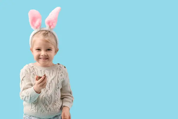 快乐的小女孩 戴着蓝色背景的巧克力蛋 长着小兔子耳朵 复活节庆祝活动 — 图库照片