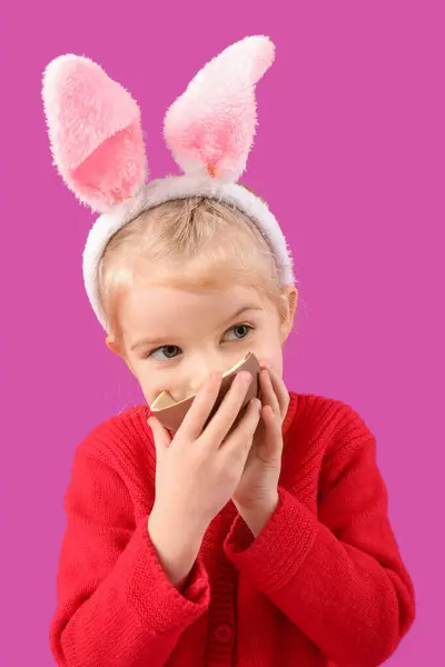 可爱的兔子耳朵小女孩吃紫色背景的巧克力蛋 复活节庆祝活动 — 图库照片
