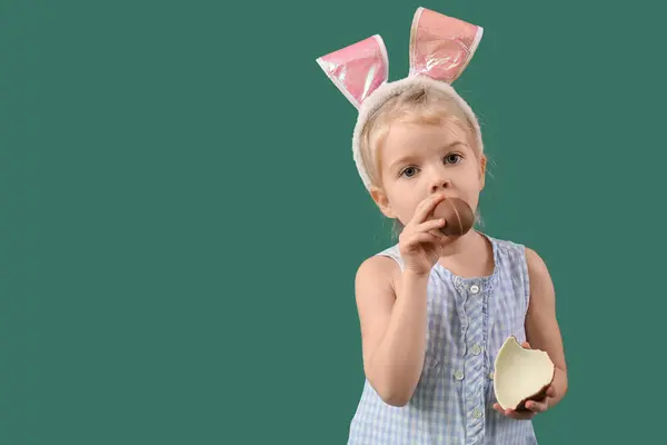 可爱的兔子耳朵小女孩吃着绿色背景的巧克力蛋 复活节庆祝活动 — 图库照片