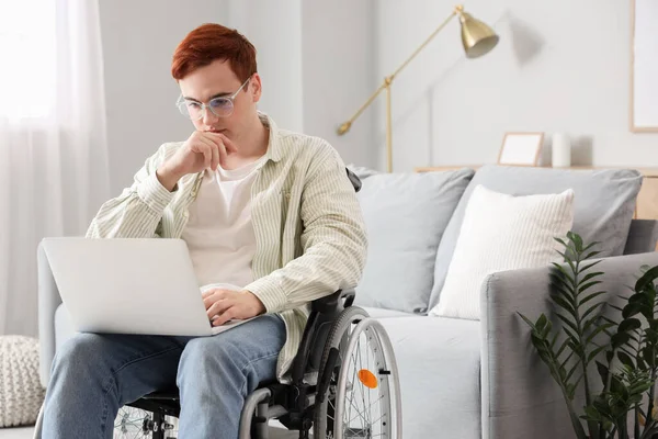 Young man in wheelchair using laptop at home