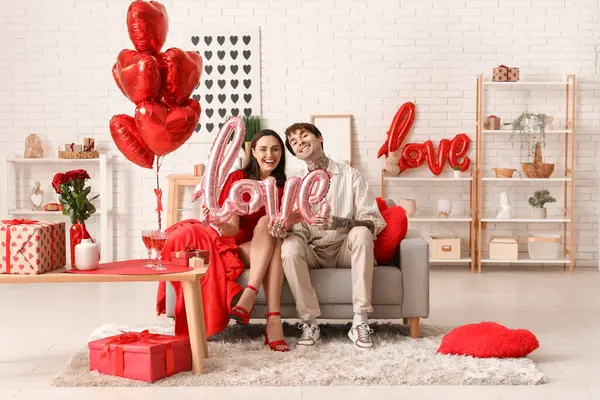 Young couple with air balloon in shape of word LOVE at home. Valentine's day celebration