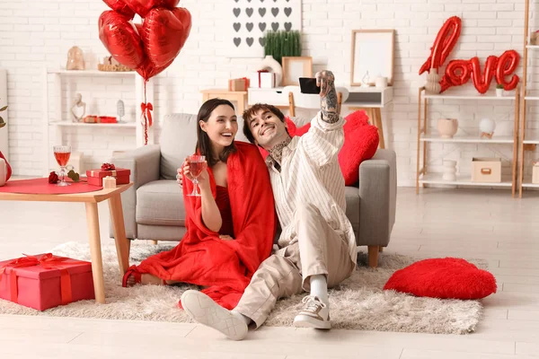 Bir bardak şarabı olan genç bir çift evde selfie çekiyor. Sevgililer Günü kutlaması