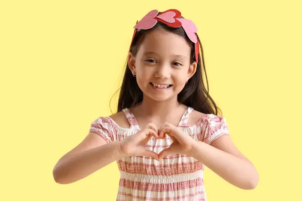 可爱的亚洲小女孩在黄色背景上做着心形 情人节庆祝活动 — 图库照片
