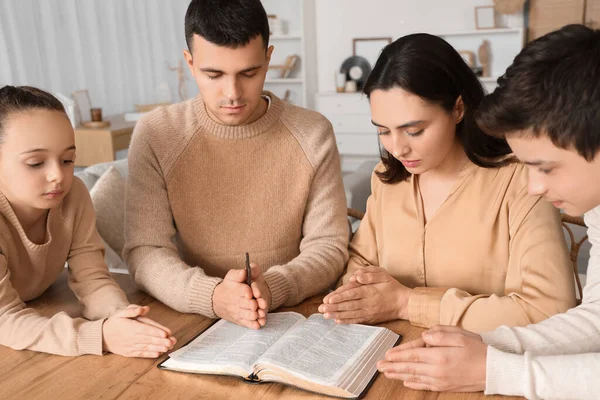 Family praying together with Holy Bible on table at home