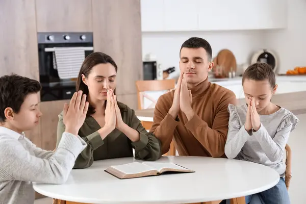 Aile mutfaktaki masada İncil ile dua ediyor.