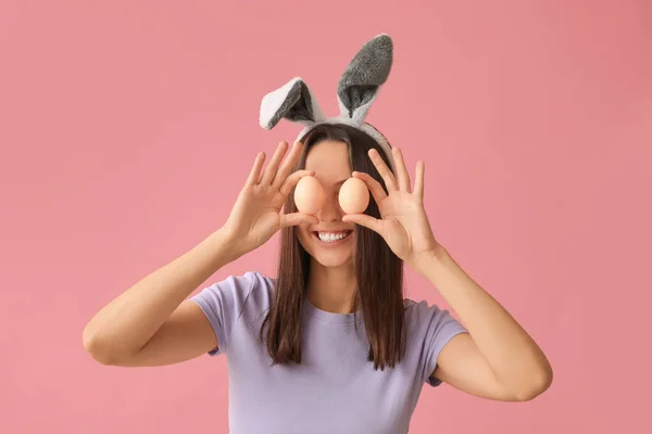 有兔子耳朵和粉色背景的复活节彩蛋的有趣的年轻女人 — 图库照片