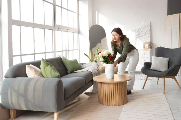 Oturma odasındaki masaya gül vazosu koyan genç bir kadın.