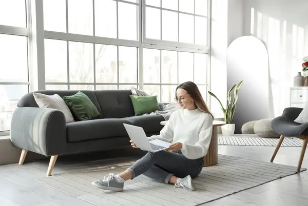 Young woman using laptop near window in living room