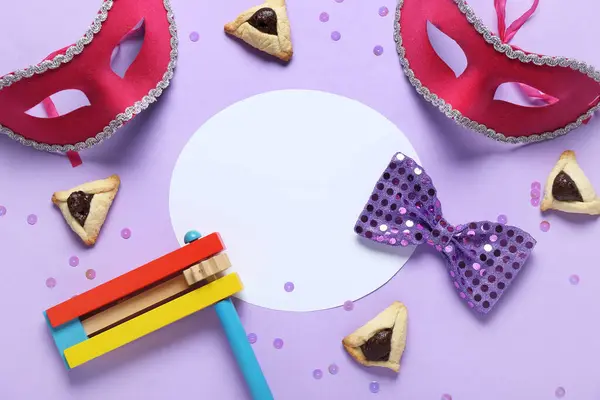 İçinde hamantaschen kurabiyeleri, karnavalın maskeleri ve Purim tatili için mor arka planda çıngırak olan boş bir kart.