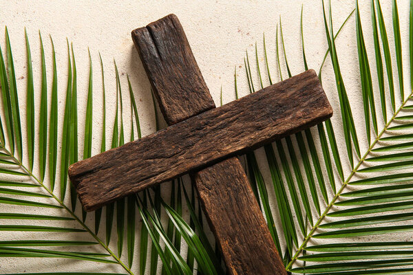 Wooden cross and palm leaves on white background