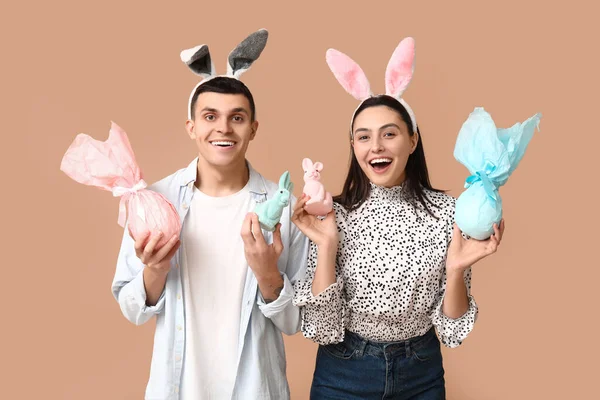 Paskalya hediyeli mutlu genç çift, oyuncak tavşanlar ve bej arka planda tavşan kulakları
