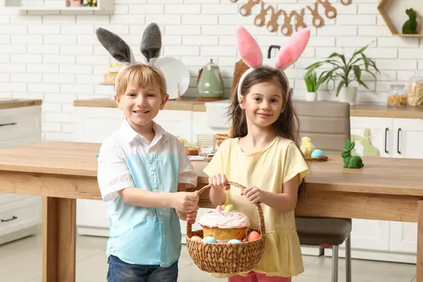 自宅でイースターエッグとケーキのバスケットとバニーの耳にかわいい小さな子供たち — ストック写真