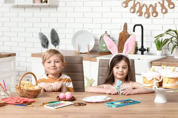 Cute little children in bunny ears painting Easter eggs at home
