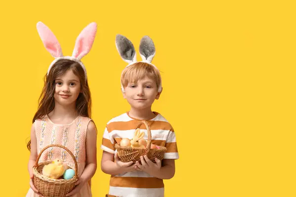 黄色の背景にイースターエッグのバスケットとバニーの耳のかわいい小さな子供たち — ストック写真