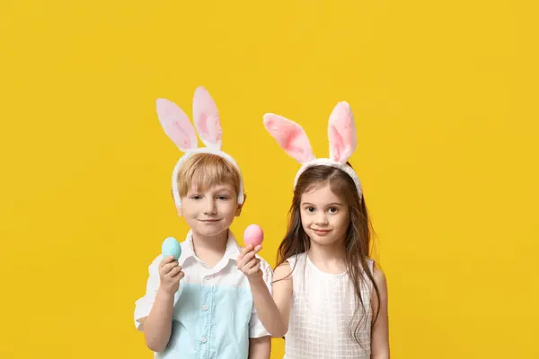黄色い背景にイースターエッグとバニー耳のかわいい小さな子供たち — ストック写真