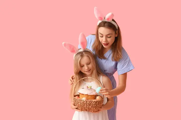 年轻的女人和她的女儿戴着兔子耳朵 手里拿着一篮子涂有粉色背景彩蛋的复活节蛋糕 — 图库照片